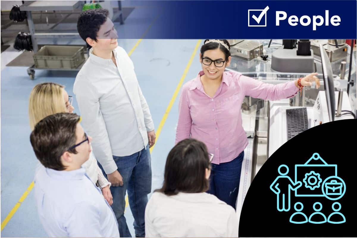 Federal Elec Blog-10 Graphic-1 A cross-functional EMS team meeting on a manufacturing floor, reviewing production requirements and supplier updates.