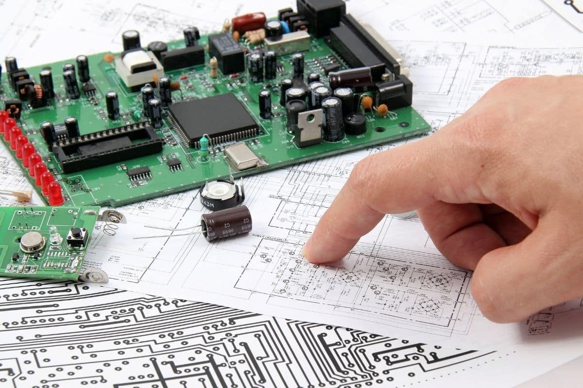 Federal Elec Blog-20 Photo-01 A person points to an electronics schematic beside an assembled circuit board and loose components.